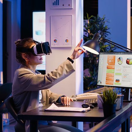 A woman uses VR goggles and gestures at a screen with charts.